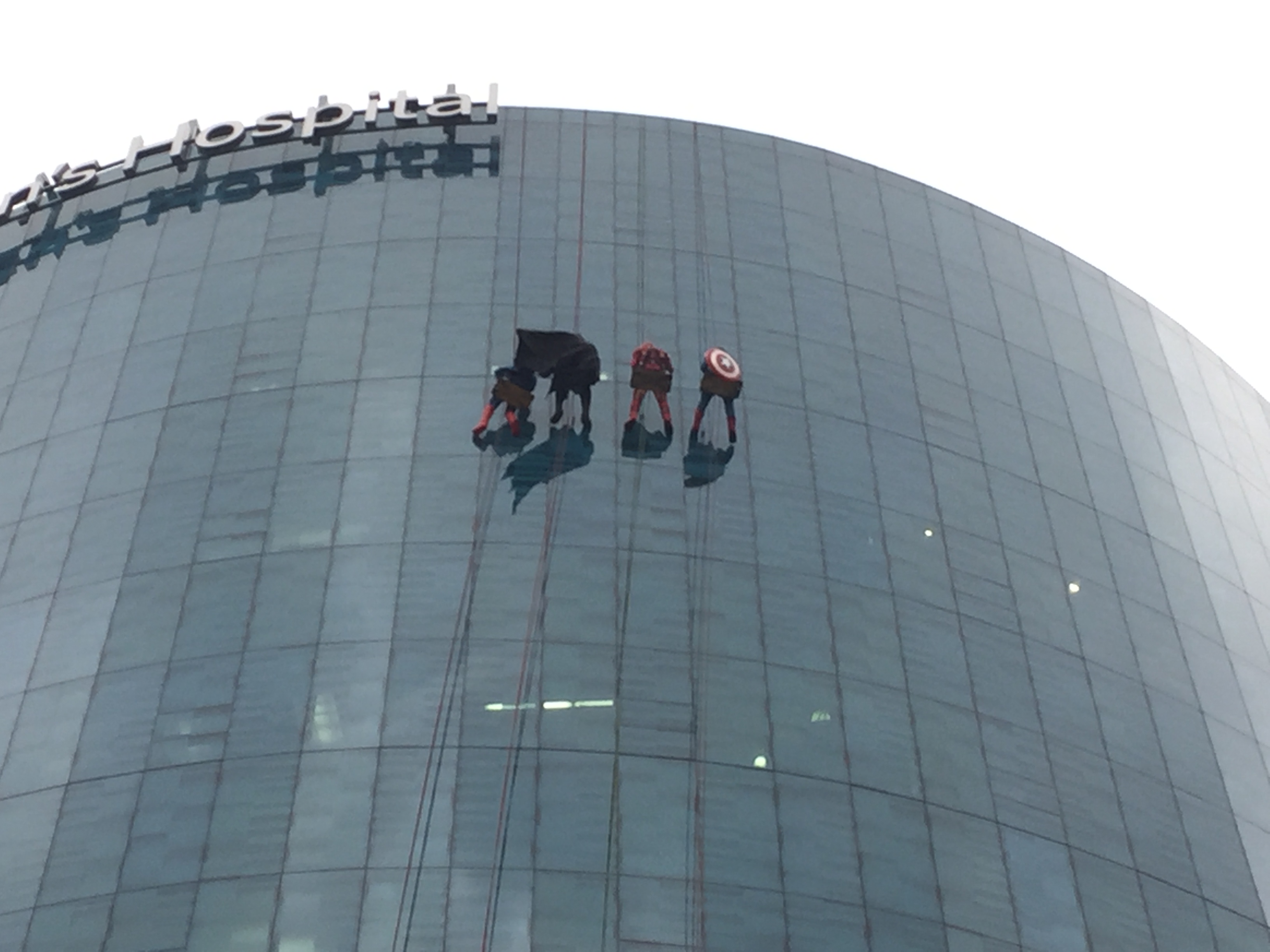 Window washers dressed as superheroes rappel down the side of the Helen Devos Children's Hospital to wave at children on Halloween
